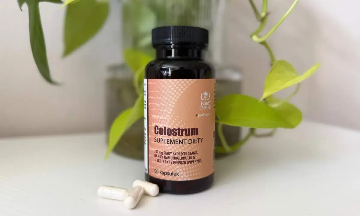 Suplement diety Colostrum w kapsułkach. Dowiedz się, colostrum co to jest i jak działa. W tle zielone liście.