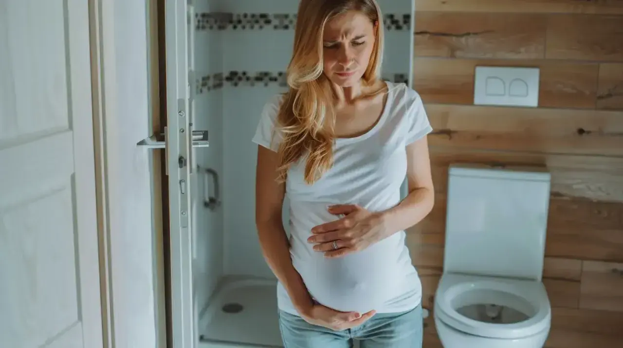 Kobieta w ciąży trzyma się za brzuch, zmartwiona. Czy na początku ciąży boli brzuch jak przy okresie?