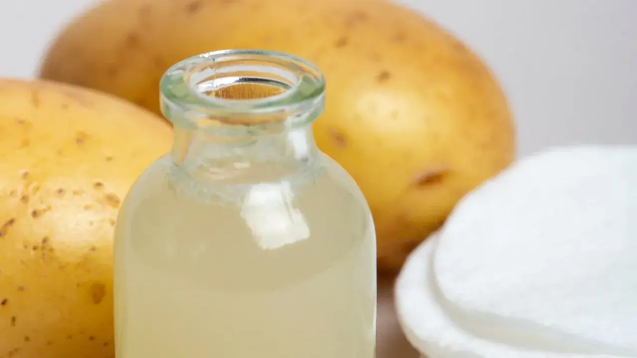 Naturalny sok z ziemniaka w buteleczce, obok surowych ziemniaków i wacików. Idealny do domowych zabiegów pielęgnacyjnych.