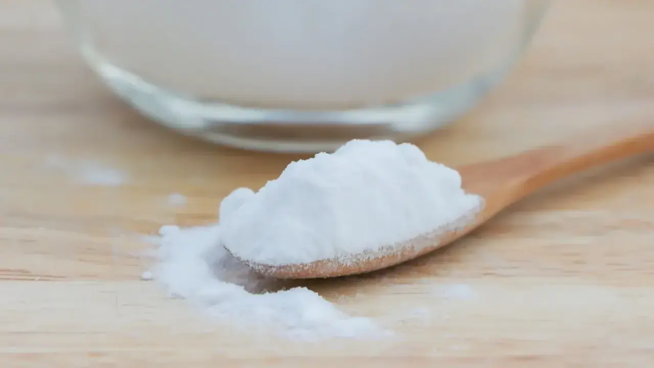 Łyżka z białym proszkiem, który może pomóc na zgagę. W tle szklana miska z tym samym produktem.