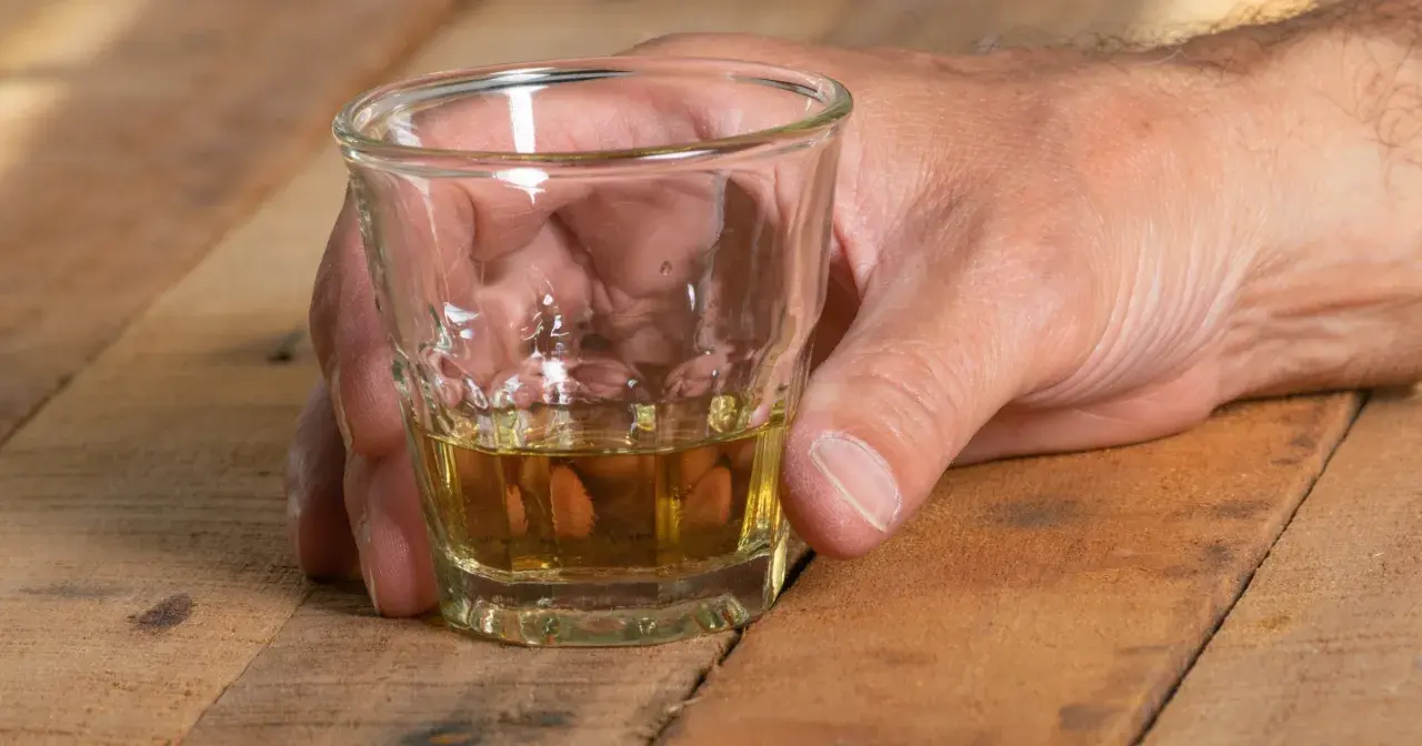 Dłoń trzyma kieliszek z bursztynowym płynem. Czy alkohol podnosi ciśnienie? To pytanie nurtuje wielu, gdy sięgają po taki trunek.