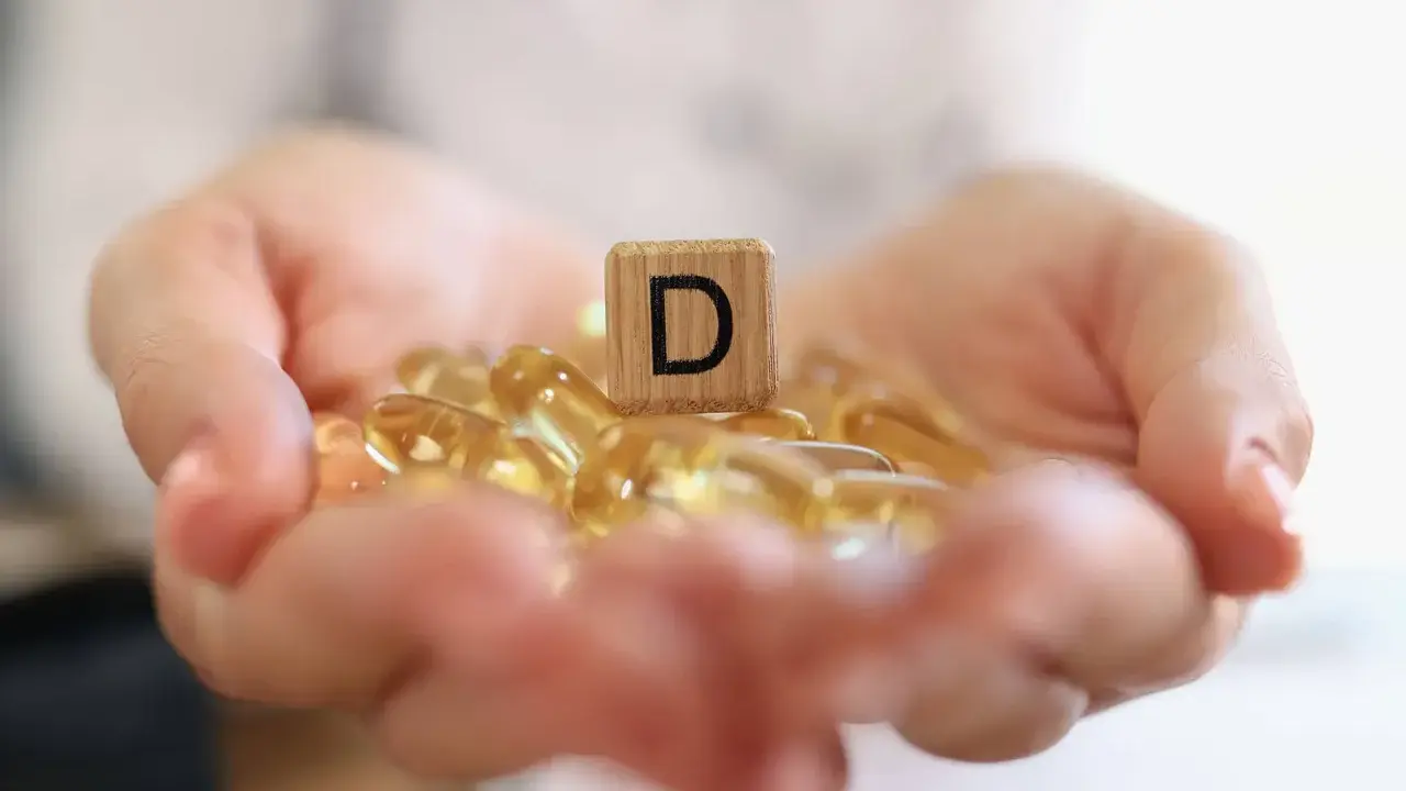 Dłonie trzymające kapsułki z witaminą D3. Drewniany klocek z literą "D" symbolizuje witamina d3 dawka uderzeniowa.