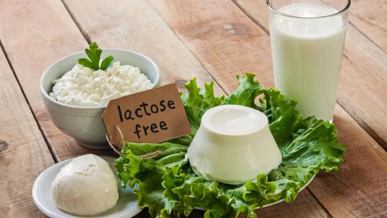 Serek wiejski, kulka sera i szklanka mleka na drewnianym stole. Etykieta "lactose free" wyjaśnia, co to jest laktoza – cukier mleczny, którego tu nie znajdziemy.