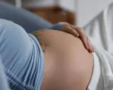 Dłoń spoczywa na **twardym brzuchu w ciąży**, ozdobionym delikatnym tatuażem.