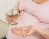 Kobieta w ciąży trzyma tabletkę i szklankę wody, szukając odpowiedzi na pytanie: co na ból głowy w ciąży.
