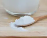 Łyżka z białym proszkiem, który może pomóc na zgagę. W tle szklana miska z tym samym produktem.