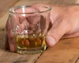 Dłoń trzyma kieliszek z bursztynowym płynem. Czy alkohol podnosi ciśnienie? To pytanie nurtuje wielu, gdy sięgają po taki trunek.