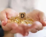 Dłonie trzymające kapsułki z witaminą D3. Drewniany klocek z literą "D" symbolizuje witamina d3 dawka uderzeniowa.