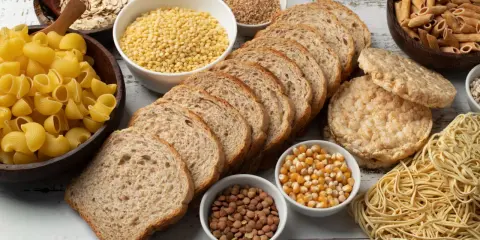 Stół pełen produktów, co ma dużo węglowodanów: makarony, płatki owsiane, chleb, ryż, kasza, kukurydza, soczewica.