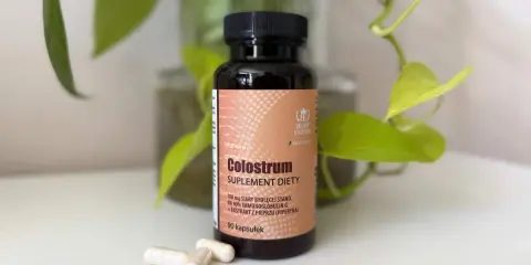 Suplement diety Colostrum w kapsułkach. Dowiedz się, colostrum co to jest i jak działa. W tle zielone liście.