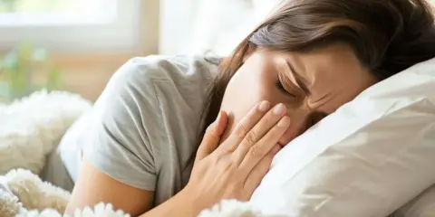 Kobieta w łóżku zakrywa usta dłonią, kaszląc. Czy zapalenie płuc jest zaraźliwe?