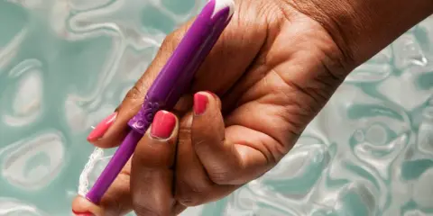 Dłoń z różowym lakierem trzyma fioletowy aplikator tamponu. Pokazuje, jak włożyć tampon, przygotowując go do użycia.