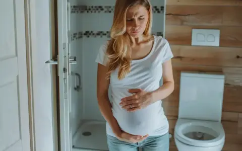 Kobieta w ciąży trzyma się za brzuch, zmartwiona. Czy na początku ciąży boli brzuch jak przy okresie?
