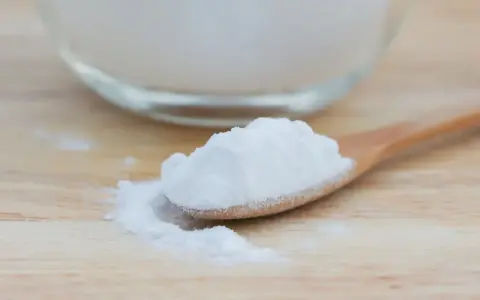 Łyżka z białym proszkiem, który może pomóc na zgagę. W tle szklana miska z tym samym produktem.