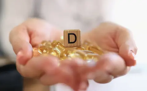 Dłonie trzymające kapsułki z witaminą D3. Drewniany klocek z literą "D" symbolizuje witamina d3 dawka uderzeniowa.