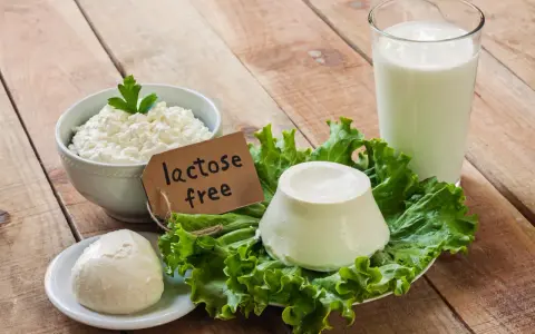 Serek wiejski, kulka sera i szklanka mleka na drewnianym stole. Etykieta "lactose free" wyjaśnia, co to jest laktoza – cukier mleczny, którego tu nie znajdziemy.