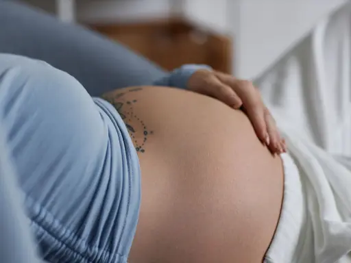 Dłoń spoczywa na **twardym brzuchu w ciąży**, ozdobionym delikatnym tatuażem.