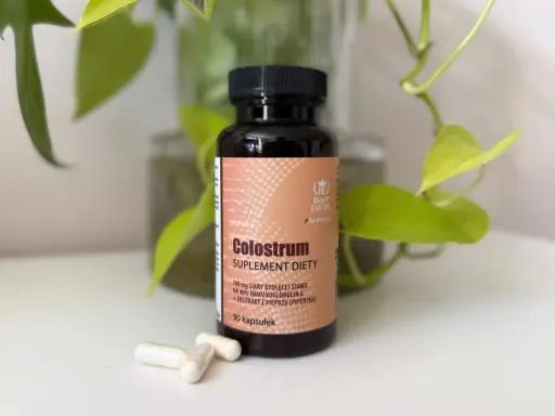 Suplement diety Colostrum w kapsułkach. Dowiedz się, colostrum co to jest i jak działa. W tle zielone liście.