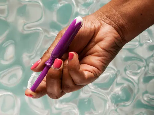 Dłoń z różowym lakierem trzyma fioletowy aplikator tamponu. Pokazuje, jak włożyć tampon, przygotowując go do użycia.