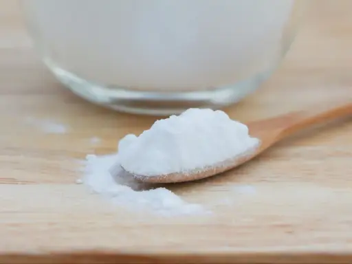 Łyżka z białym proszkiem, który może pomóc na zgagę. W tle szklana miska z tym samym produktem.