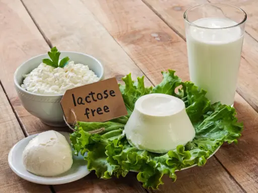 Serek wiejski, kulka sera i szklanka mleka na drewnianym stole. Etykieta "lactose free" wyjaśnia, co to jest laktoza – cukier mleczny, którego tu nie znajdziemy.