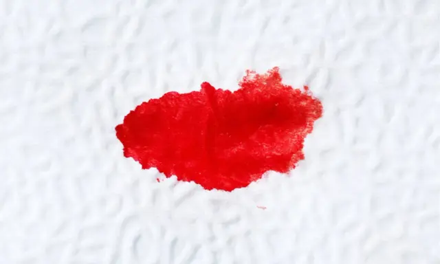 Plama krwi na białym materiale, przypominająca ślady po problemach z odbytem.