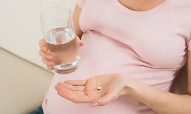 Kobieta w ciąży trzyma tabletkę i szklankę wody, szukając odpowiedzi na pytanie: co na ból głowy w ciąży.