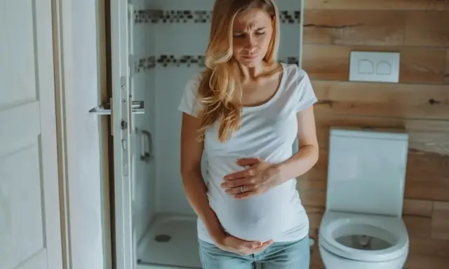 Kobieta w ciąży trzyma się za brzuch, zmartwiona. Czy na początku ciąży boli brzuch jak przy okresie?