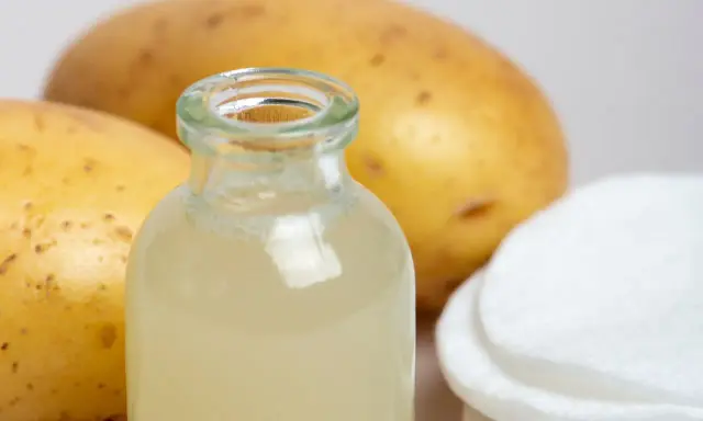 Naturalny sok z ziemniaka w buteleczce, obok surowych ziemniaków i wacików. Idealny do domowych zabiegów pielęgnacyjnych.