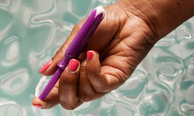 Dłoń z różowym lakierem trzyma fioletowy aplikator tamponu. Pokazuje, jak włożyć tampon, przygotowując go do użycia.