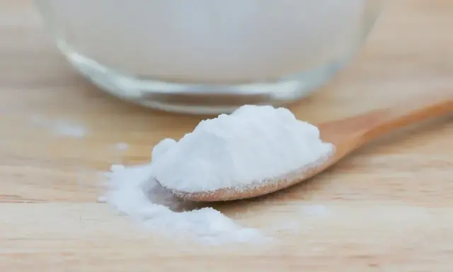 Łyżka z białym proszkiem, który może pomóc na zgagę. W tle szklana miska z tym samym produktem.
