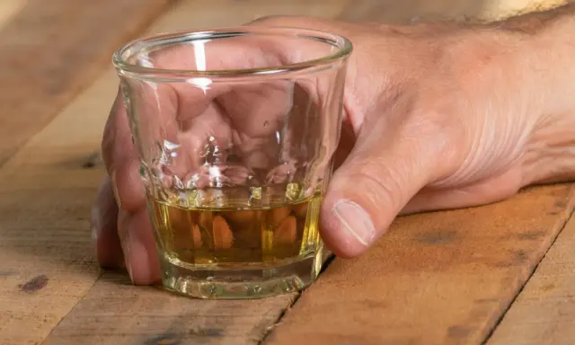 Dłoń trzyma kieliszek z bursztynowym płynem. Czy alkohol podnosi ciśnienie? To pytanie nurtuje wielu, gdy sięgają po taki trunek.