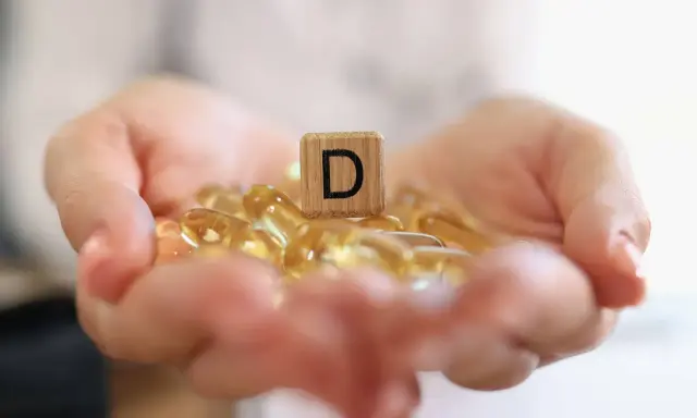 Dłonie trzymające kapsułki z witaminą D3. Drewniany klocek z literą "D" symbolizuje witamina d3 dawka uderzeniowa.
