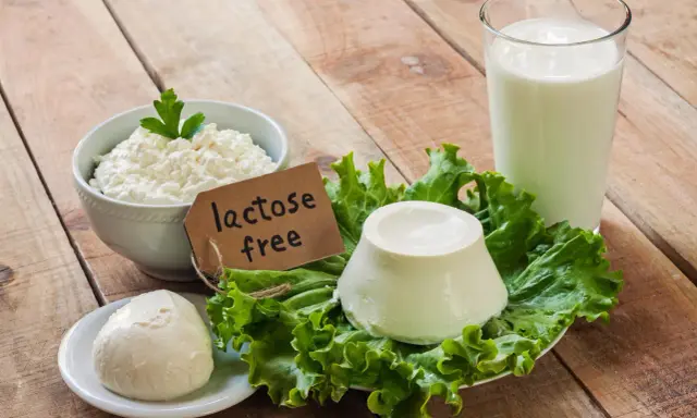 Serek wiejski, kulka sera i szklanka mleka na drewnianym stole. Etykieta "lactose free" wyjaśnia, co to jest laktoza – cukier mleczny, którego tu nie znajdziemy.