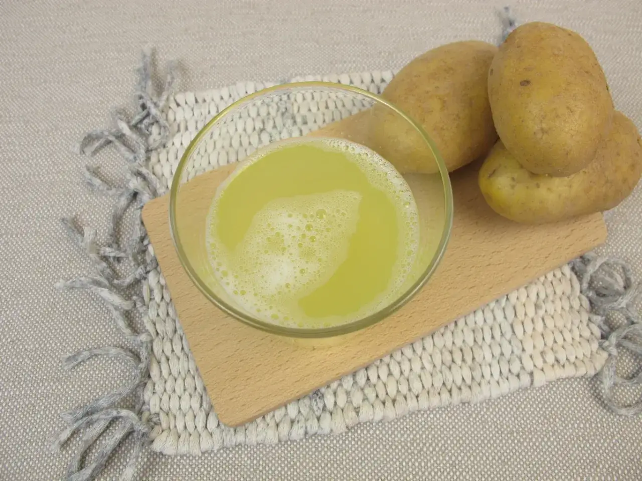 Szklanka z pianistym sokiem z ziemniaka obok świeżych bulw. Naturalny napój na drewnianej desce.