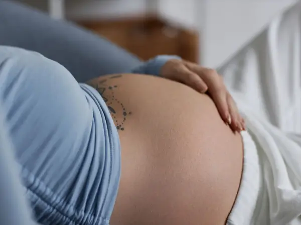 Dłoń spoczywa na **twardym brzuchu w ciąży**, ozdobionym delikatnym tatuażem.